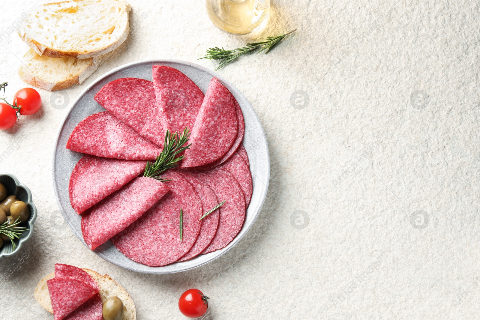 Slices of delicious sausage with rosemary served on white textured table, flat lay. Space for text Photo of Slices of delicious sausage with rosemary served on white textured table, flat lay. Space for text