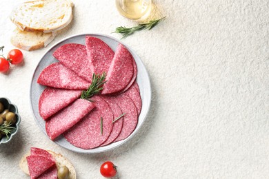 Photo of Slices of delicious sausage with rosemary served on white textured table, flat lay. Space for text