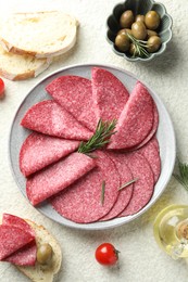 Photo of Slices of delicious sausage with rosemary served on white textured table, flat lay