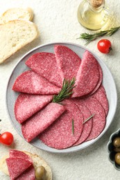 Photo of Slices of delicious sausage with rosemary served on white textured table, flat lay