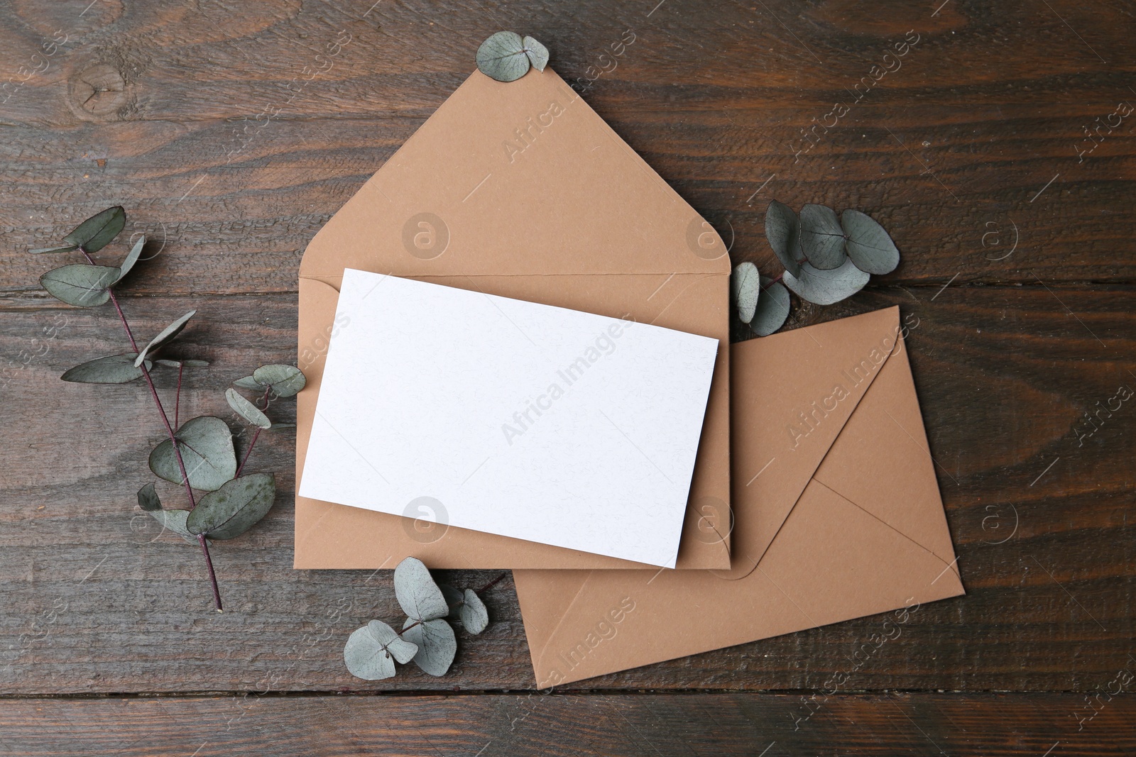 Blank greeting card, paper envelopes and eucalyptus leaves on wooden table, flat lay Photo of Blank greeting card, paper envelopes and eucalyptus leaves on wooden table, flat lay