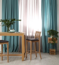 Photo of Stylish wooden table and chairs near window with elegant curtains in room