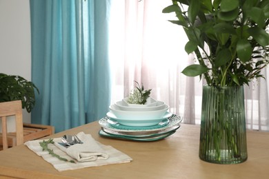 Photo of Dishware and plants on wooden table near window with elegant curtains