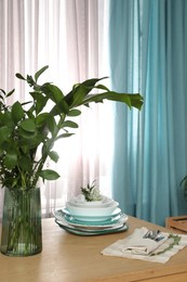 Photo of Dishware and plants on wooden table near window with elegant curtains