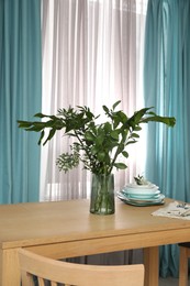 Photo of Dishware and plants on wooden table near window with elegant curtains