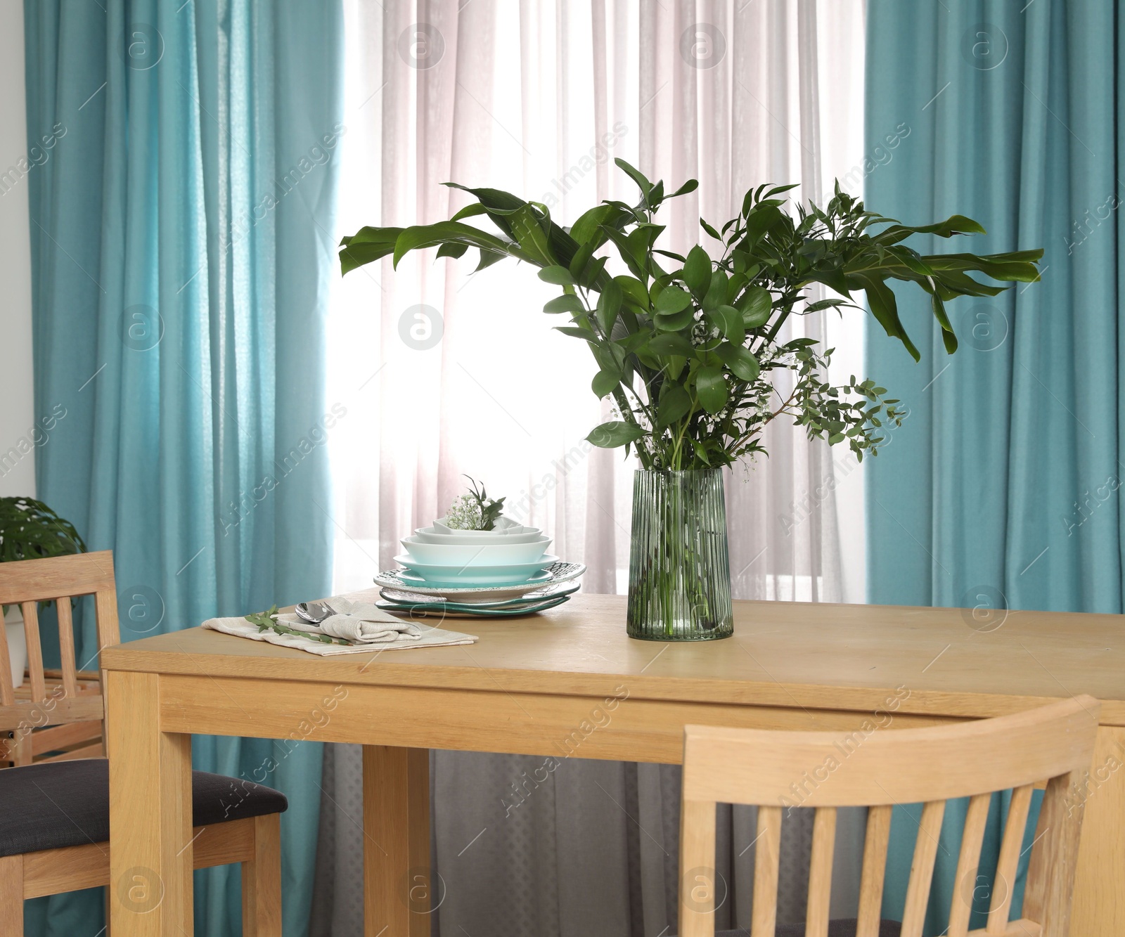 Photo of Dishware and plants on wooden table near window with open curtains