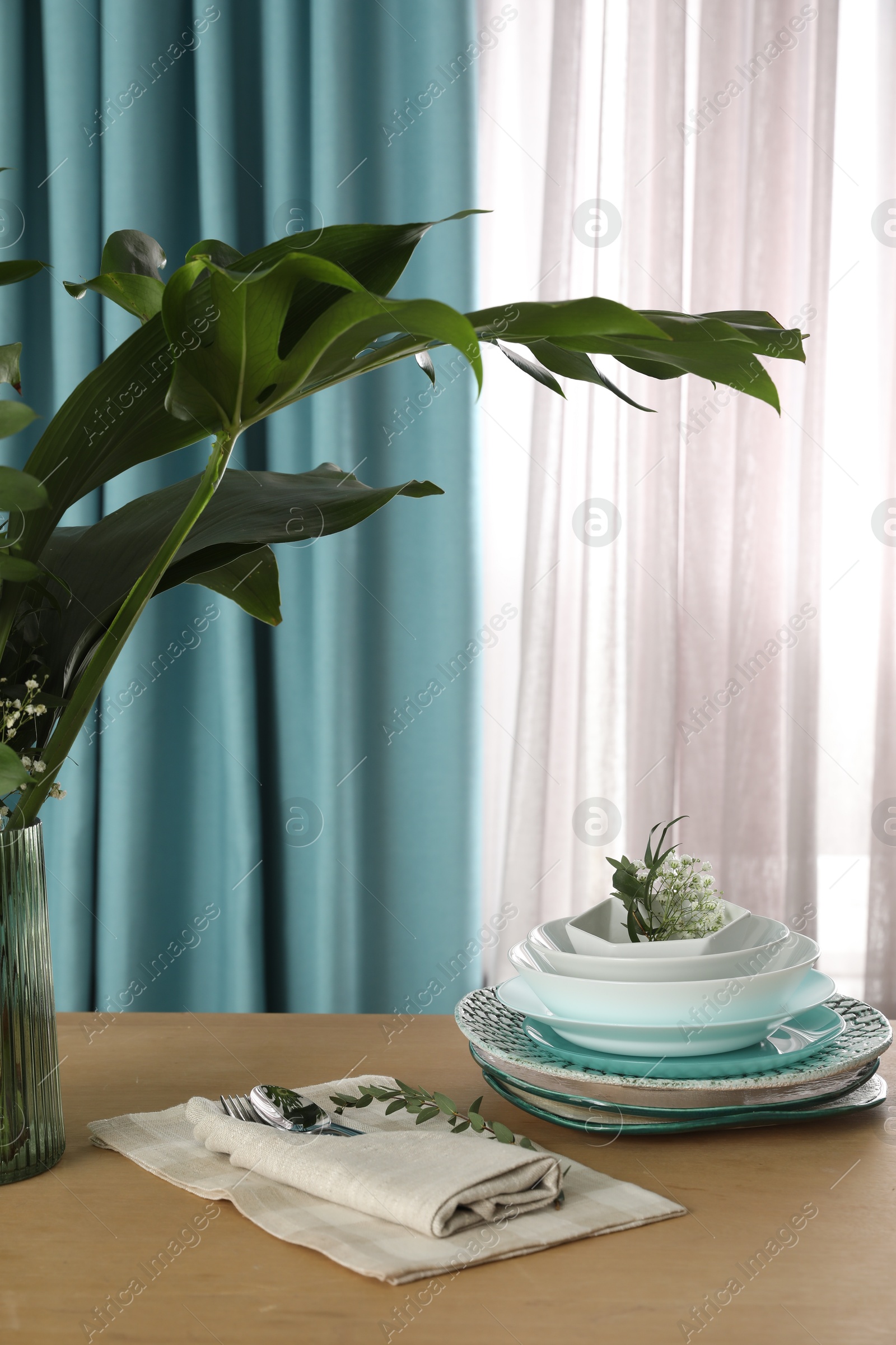 Dishware on wooden table near window with elegant curtains Photo of Dishware on wooden table near window with elegant curtains