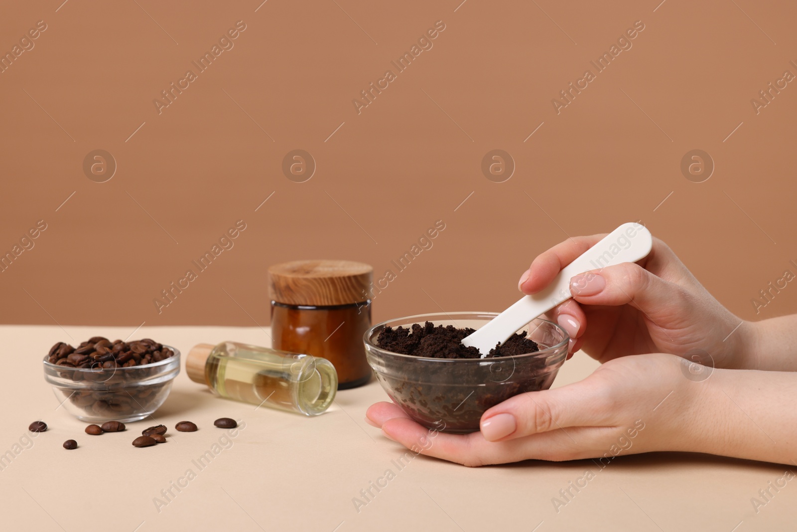 Woman with bowl of body scrub against dark beige background, closeup Photo of Woman with bowl of body scrub against dark beige background, closeup