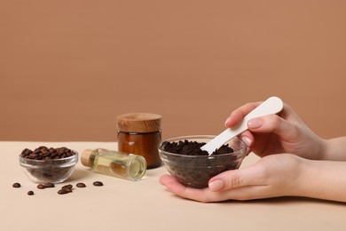 Photo of Woman with bowl of body scrub against dark beige background, closeup
