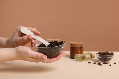 Photo of Woman with bowl of body scrub against dark beige background, closeup