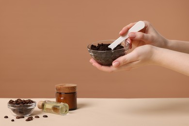 Photo of Woman with bowl of body scrub against dark beige background, closeup