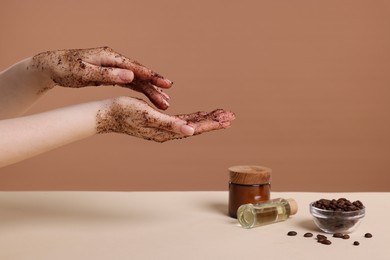 Photo of Woman applying body scrub onto her hand against dark beige background, closeup