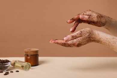 Photo of Woman applying body scrub onto her hand against dark beige background, closeup
