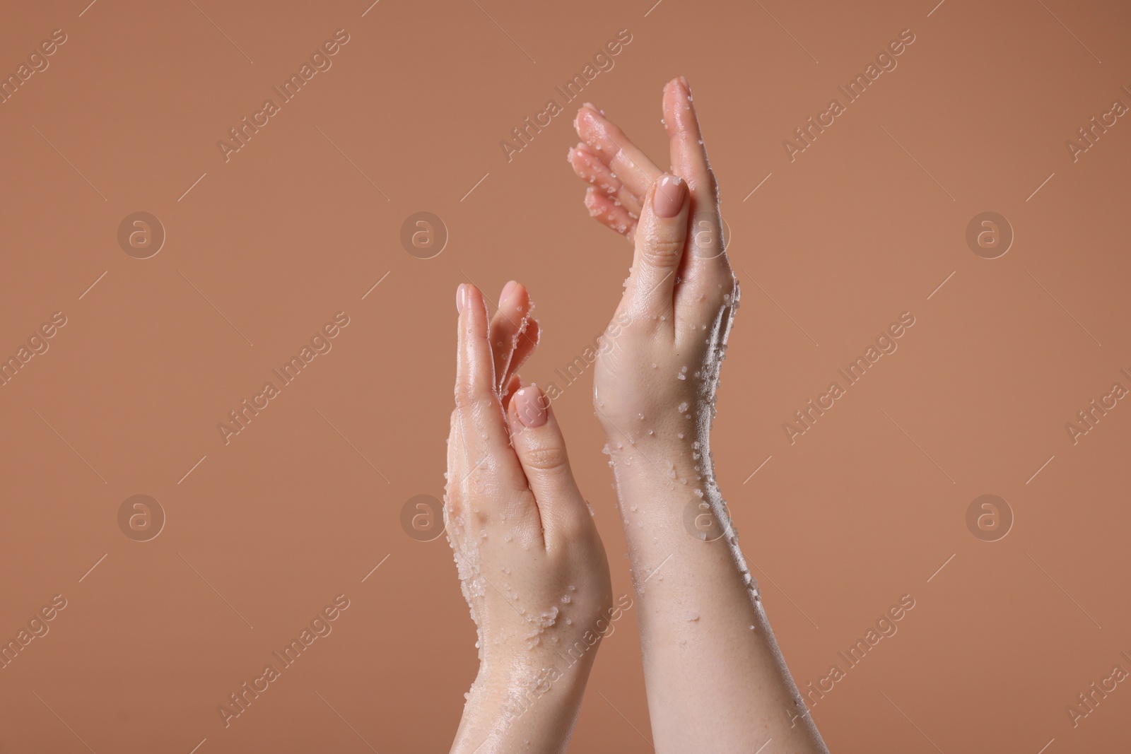 Woman applying body scrub onto her hand against dark beige background, closeup Photo of Woman applying body scrub onto her hand against dark beige background, closeup