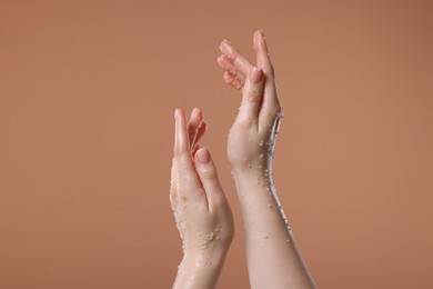 Photo of Woman applying body scrub onto her hand against dark beige background, closeup
