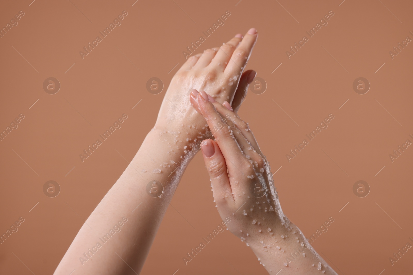 Woman applying body scrub onto her hand against dark beige background, closeup Photo of Woman applying body scrub onto her hand against dark beige background, closeup
