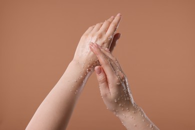 Photo of Woman applying body scrub onto her hand against dark beige background, closeup