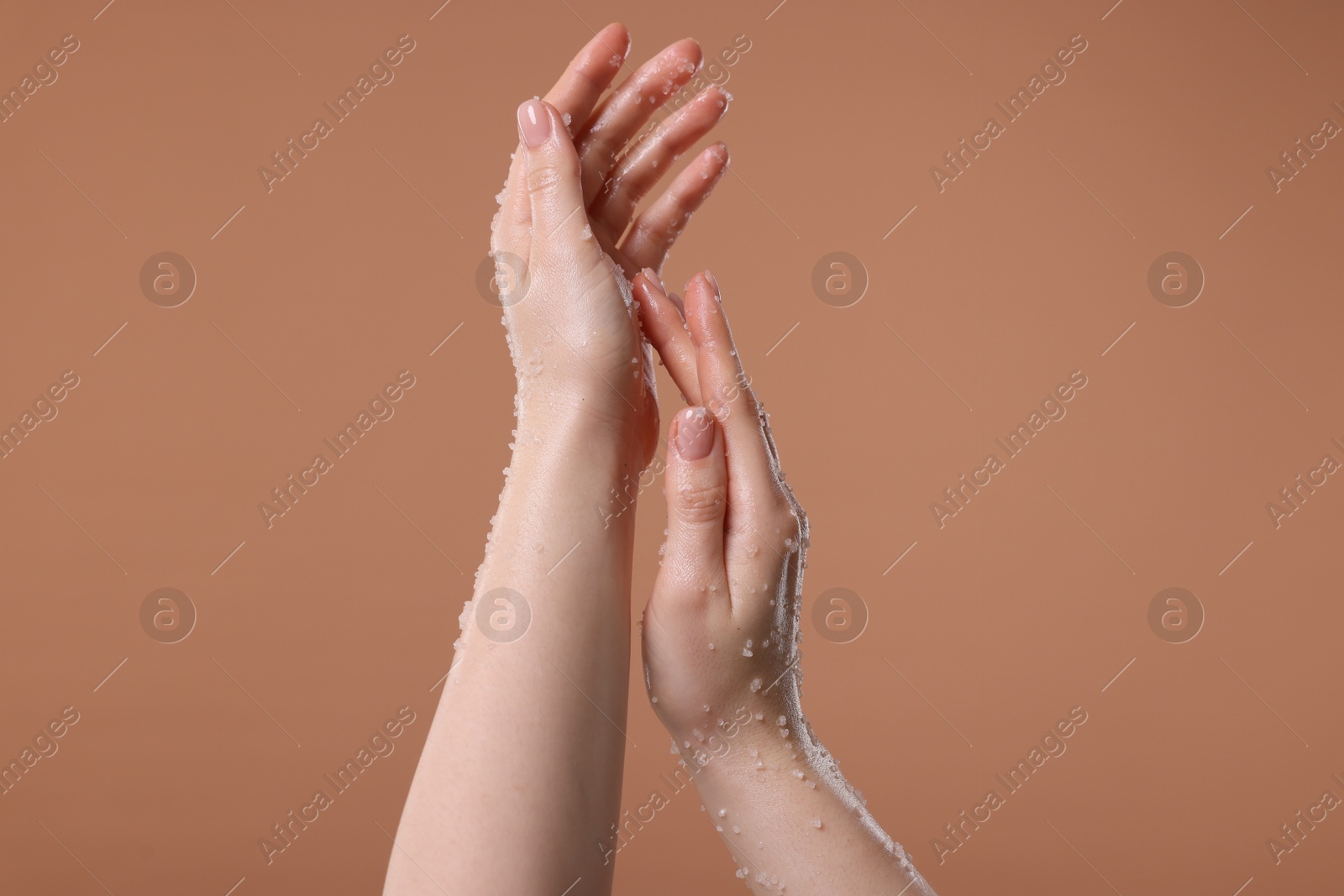 Woman applying body scrub onto her hand against dark beige background, closeup Photo of Woman applying body scrub onto her hand against dark beige background, closeup