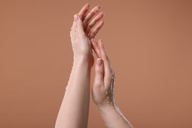 Photo of Woman applying body scrub onto her hand against dark beige background, closeup