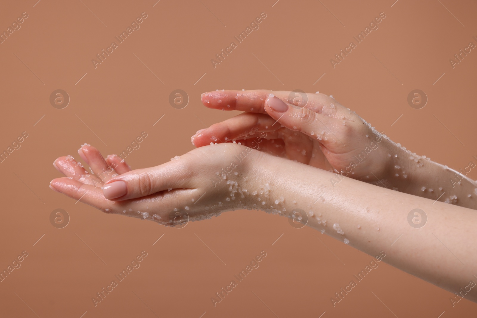 Woman applying body scrub onto her hand against dark beige background, closeup Photo of Woman applying body scrub onto her hand against dark beige background, closeup
