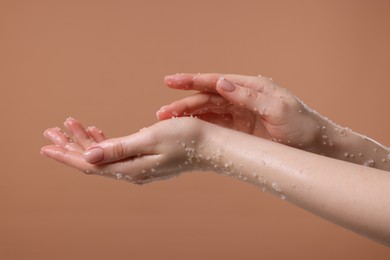 Photo of Woman applying body scrub onto her hand against dark beige background, closeup