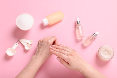 Photo of Woman applying body scrub onto her hand on pink background, top view