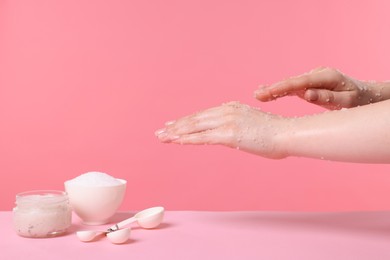 Photo of Woman applying body scrub onto her hand against pink background, closeup