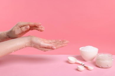 Photo of Woman applying body scrub onto her hand against pink background, closeup