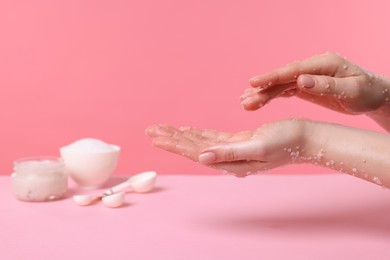 Photo of Woman applying body scrub onto her hand against pink background, closeup