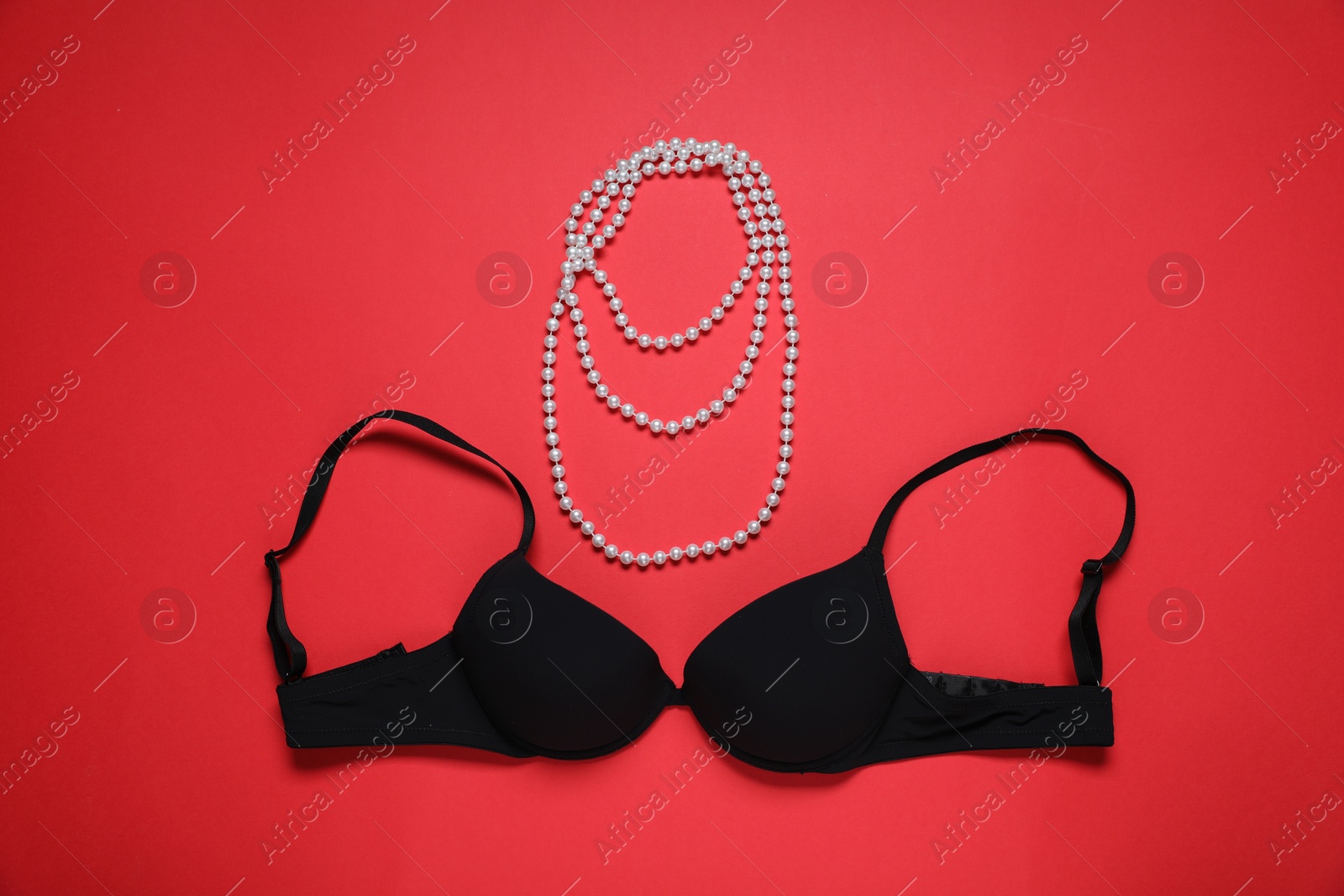 Photo of Black bra and pearl necklace on red background, flat lay