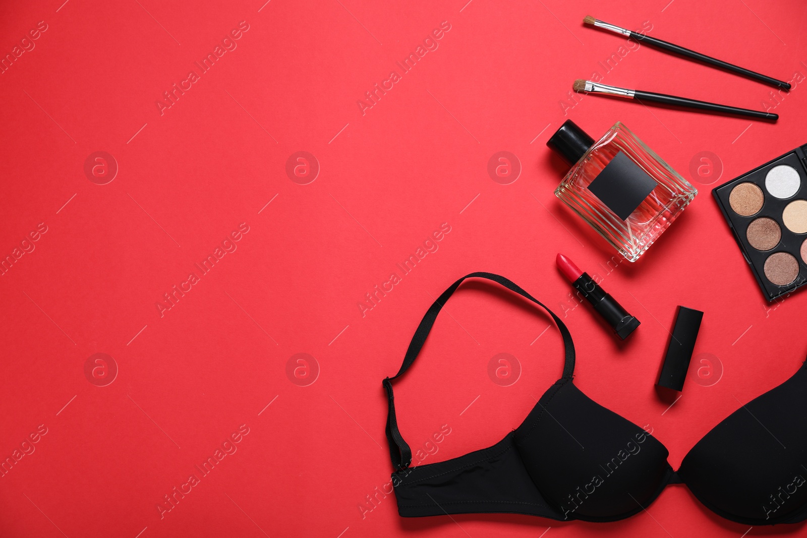Black bra, perfume and makeup products on red background, flat lay. Space for text Photo of Black bra, perfume and makeup products on red background, flat lay. Space for text