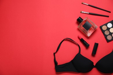 Photo of Black bra, perfume and makeup products on red background, flat lay. Space for text