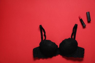 Photo of Lace bra and lipstick on red background, flat lay. Space for text