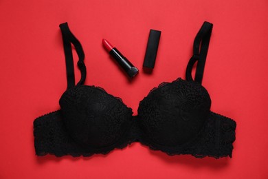Photo of Lace bra and lipstick on red background, flat lay