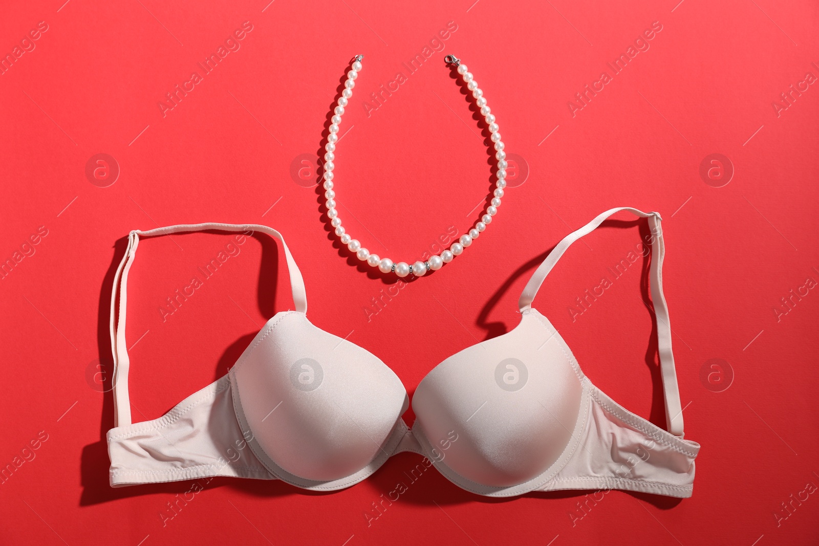 Beige bra and pearl necklace on red background, flat lay Photo of Beige bra and pearl necklace on red background, flat lay