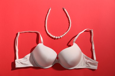 Photo of Beige bra and pearl necklace on red background, flat lay