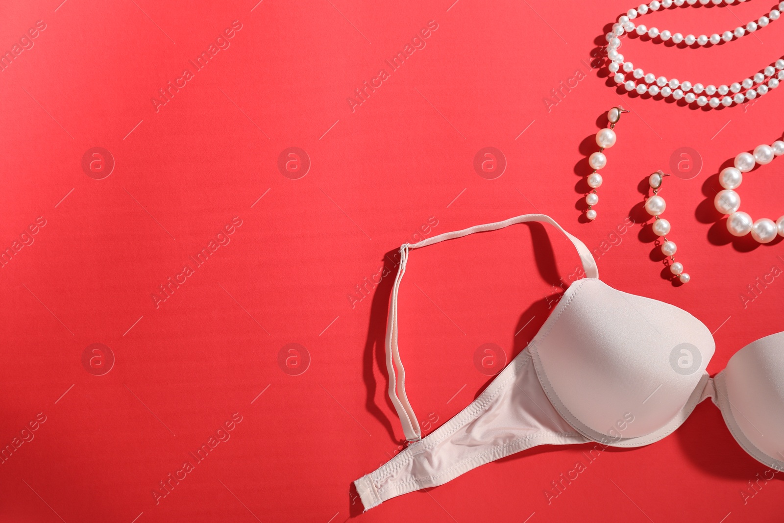 Beige bra and jewelry on red background, flat lay. Space for text Photo of Beige bra and jewelry on red background, flat lay. Space for text