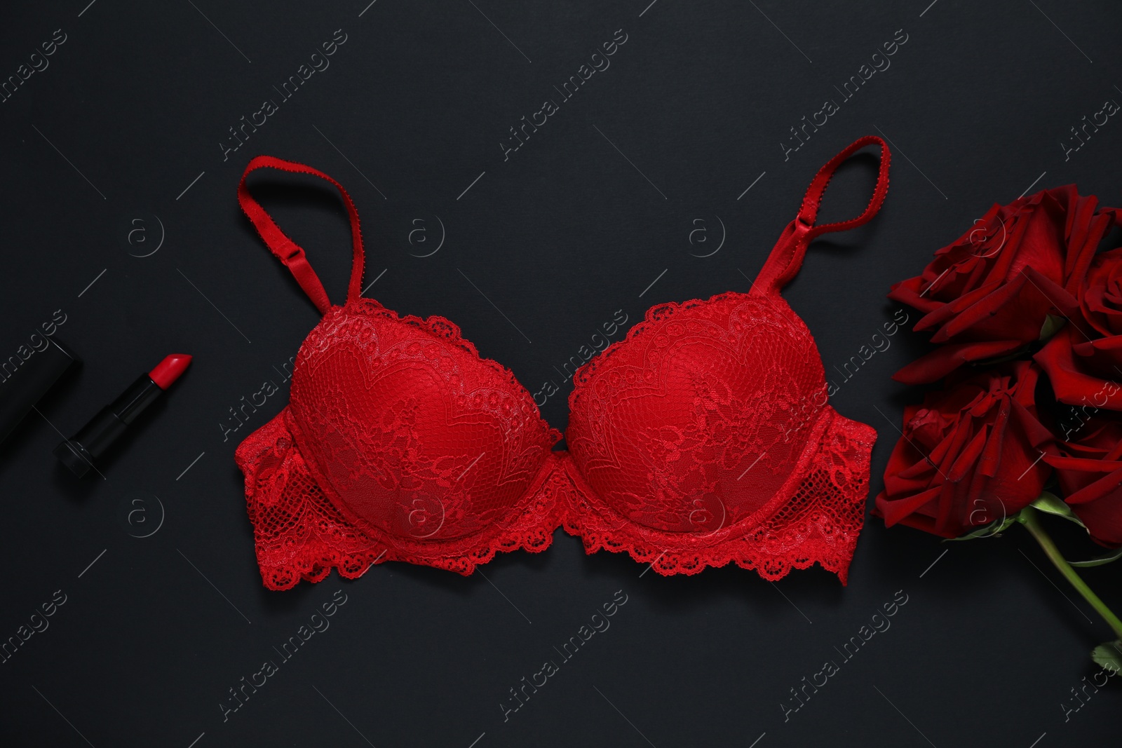 Lace bra, red roses and lipstick on black background, flat lay Photo of Lace bra, red roses and lipstick on black background, flat lay
