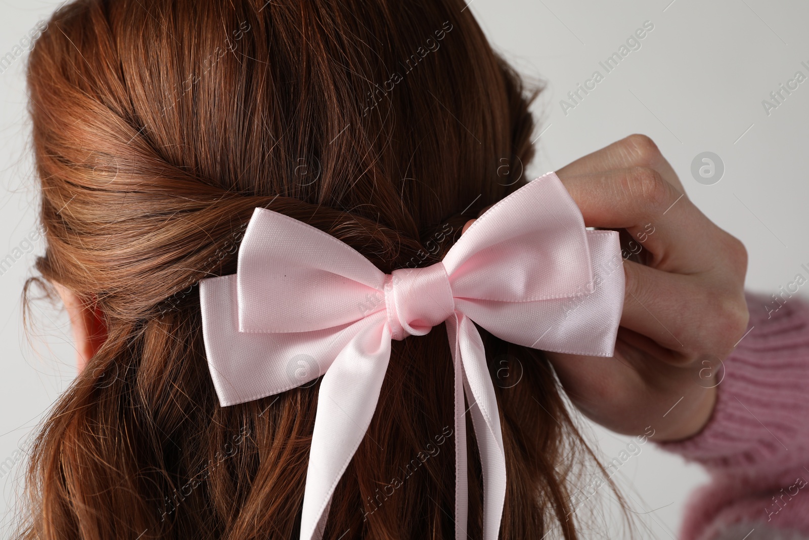 Woman with beautiful hair bow on light grey background, back view Photo of Woman with beautiful hair bow on light grey background, back view