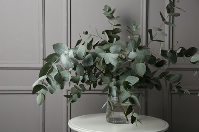 Photo of Beautiful eucalyptus branches in vase on table near grey wall indoors