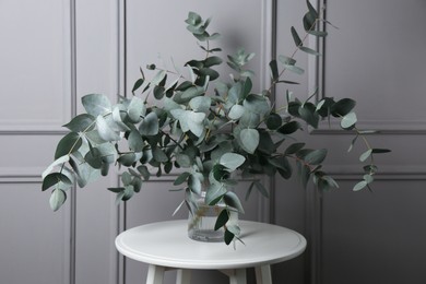 Photo of Beautiful eucalyptus branches in vase on table near grey wall indoors