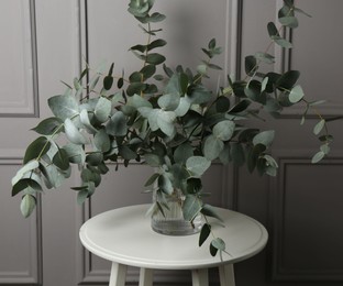 Photo of Beautiful eucalyptus branches in vase on table near grey wall indoors