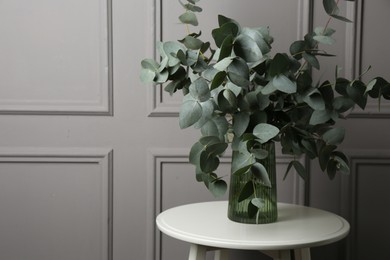 Photo of Beautiful eucalyptus branches in vase on table near grey wall indoors, space for text