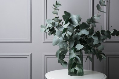 Photo of Beautiful eucalyptus branches in vase on table near grey wall indoors, space for text
