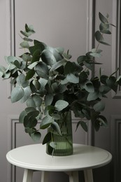 Photo of Beautiful eucalyptus branches in vase on table near grey wall indoors