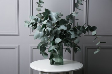 Photo of Beautiful eucalyptus branches in vase on table near grey wall indoors