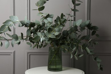 Photo of Beautiful eucalyptus branches in vase on table near grey wall indoors