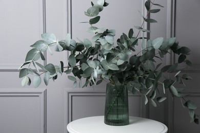 Photo of Beautiful eucalyptus branches in vase on table near grey wall indoors