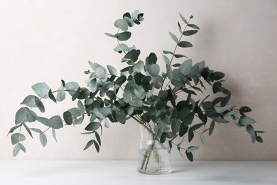 Photo of Beautiful eucalyptus branches in vase on table near light grey wall indoors