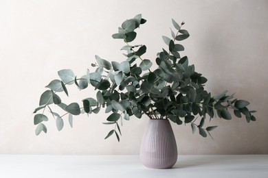 Photo of Beautiful eucalyptus branches in vase on table near light grey wall indoors